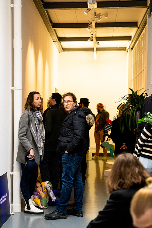 Toeschouwers staan voor de voorstelling te wachten in de smalle gang van de kunstgalerie.